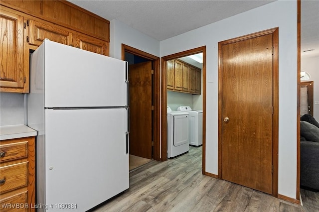 kitchen featuring brown cabinetry, washer and clothes dryer, light wood-type flooring, and freestanding refrigerator