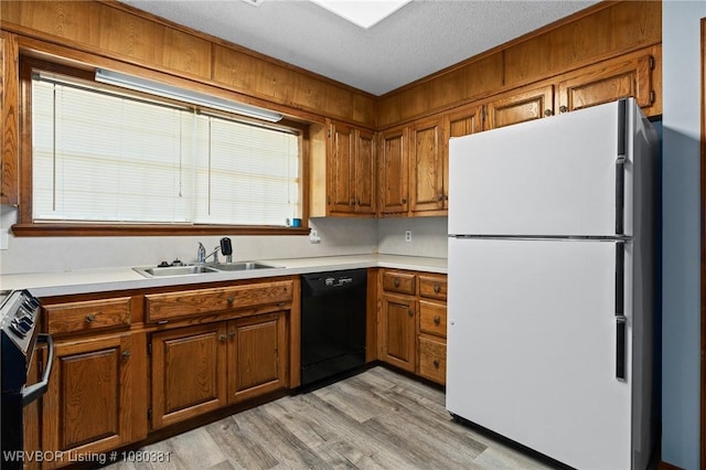 kitchen with a sink, freestanding refrigerator, black dishwasher, stainless steel stove, and brown cabinetry
