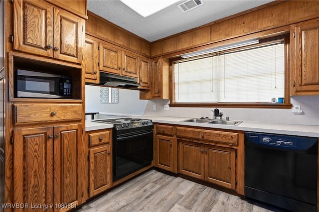 kitchen with a sink, visible vents, brown cabinetry, under cabinet range hood, and black appliances
