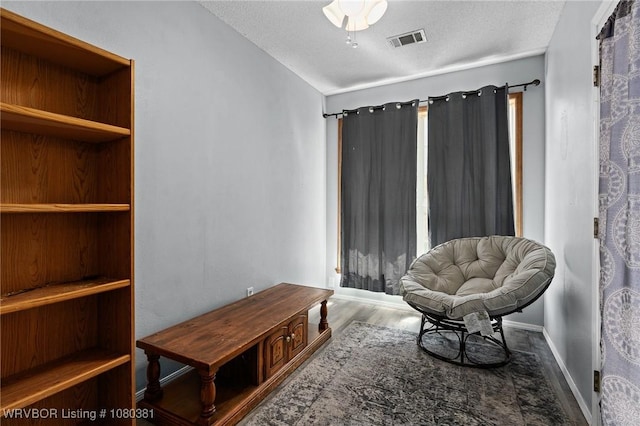 sitting room featuring baseboards, wood finished floors, visible vents, and a textured ceiling