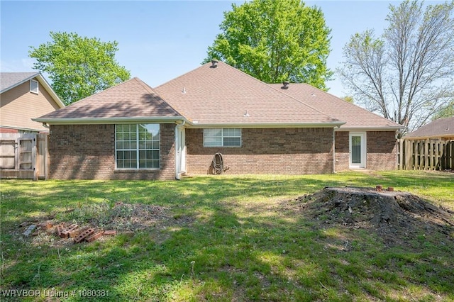 back of house with brick siding, a yard, and fence
