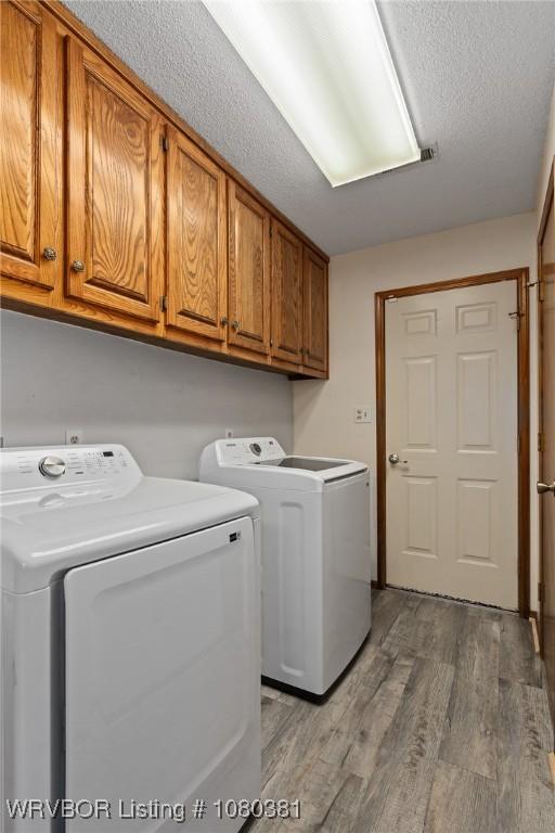 clothes washing area featuring washing machine and clothes dryer, cabinet space, wood finished floors, and a textured ceiling