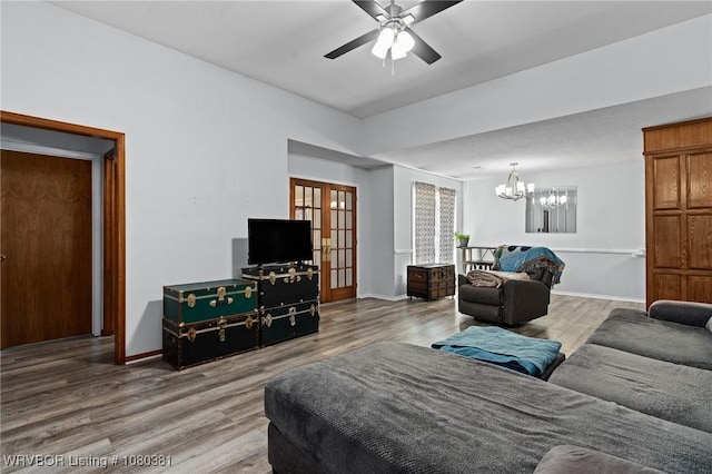 living room with ceiling fan with notable chandelier, baseboards, and wood finished floors