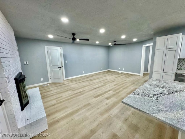 living room with ceiling fan, light hardwood / wood-style floors, a textured ceiling, and a brick fireplace