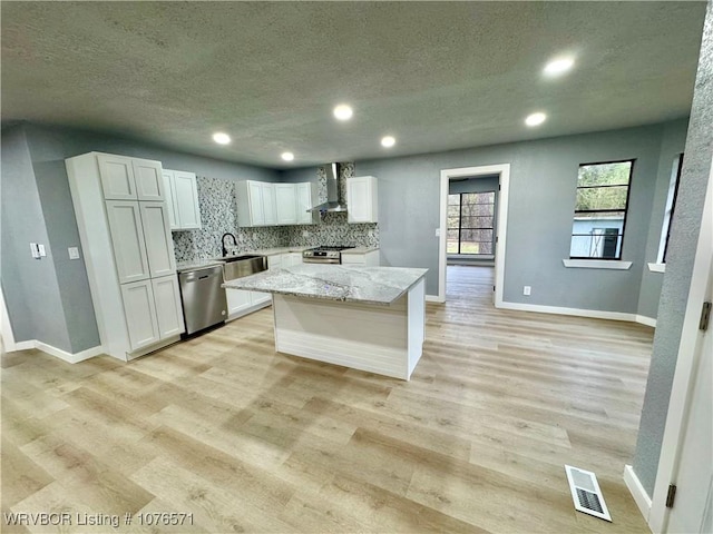 kitchen featuring appliances with stainless steel finishes, a kitchen island, white cabinetry, and wall chimney exhaust hood