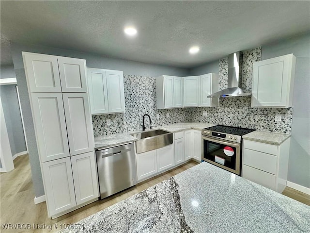 kitchen featuring wall chimney exhaust hood, sink, white cabinetry, and stainless steel appliances