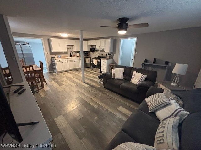 living area with light wood finished floors, ceiling fan, and a textured ceiling