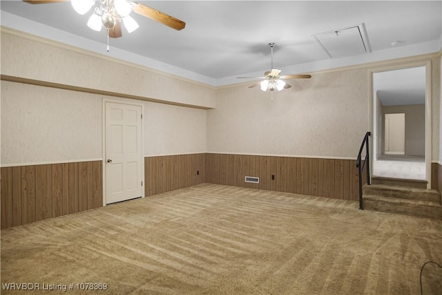 carpeted empty room featuring a wainscoted wall, wooden walls, visible vents, attic access, and ceiling fan