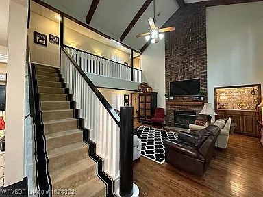 living room featuring a large fireplace, ceiling fan, wood-type flooring, high vaulted ceiling, and beamed ceiling