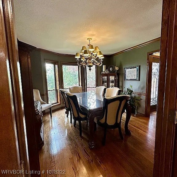 dining space featuring hardwood / wood-style flooring, ornamental molding, a textured ceiling, and a chandelier