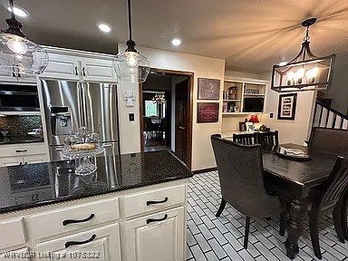 kitchen with stainless steel fridge with ice dispenser, decorative light fixtures, white cabinetry, and dark stone countertops