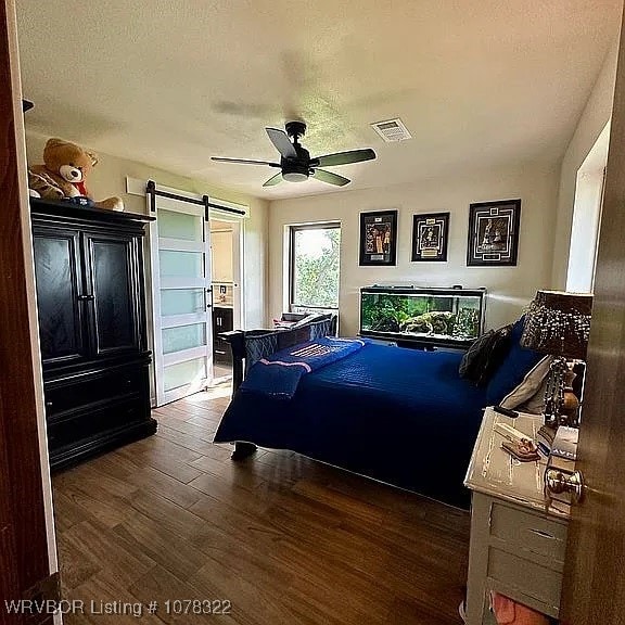 bedroom with a textured ceiling, a barn door, ceiling fan, and dark hardwood / wood-style floors