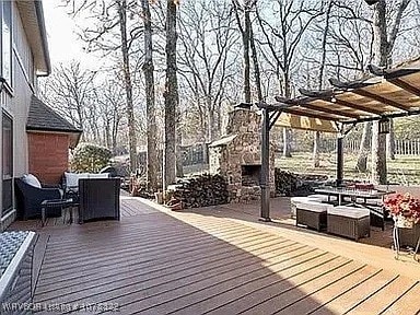 wooden terrace with an outdoor stone fireplace and a pergola