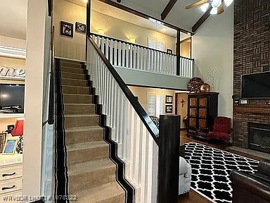 staircase with a towering ceiling, a brick fireplace, and ceiling fan