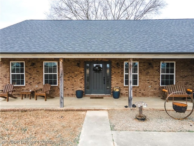 exterior space with brick siding, a patio, and roof with shingles