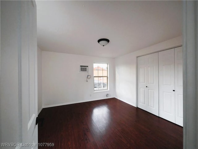 unfurnished bedroom with dark hardwood / wood-style flooring, a wall unit AC, and a closet