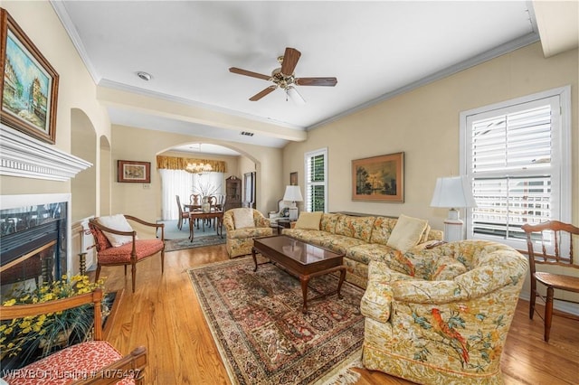 living room featuring a high end fireplace, light hardwood / wood-style floors, ceiling fan with notable chandelier, and ornamental molding