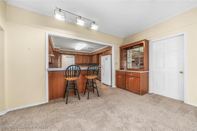 kitchen featuring a kitchen breakfast bar, light colored carpet, white fridge with ice dispenser, and crown molding