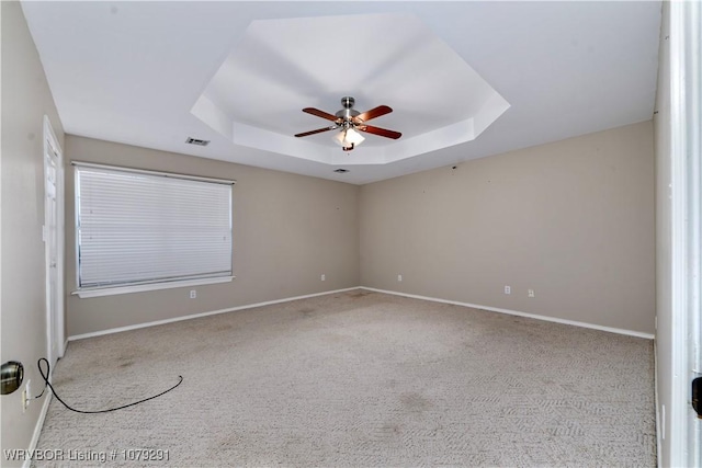 carpeted spare room with ceiling fan, a tray ceiling, visible vents, and baseboards