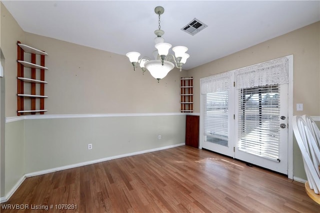 interior space featuring baseboards, visible vents, a chandelier, and wood finished floors