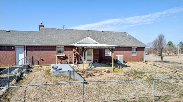 rear view of property featuring a shingled roof, a fenced backyard, brick siding, and central air condition unit