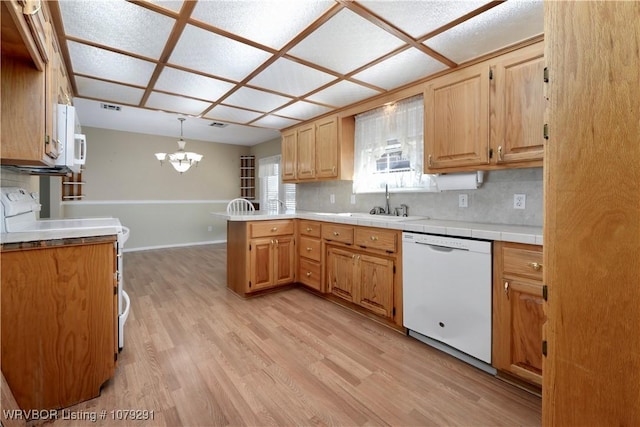 kitchen featuring light wood finished floors, backsplash, a sink, white appliances, and a peninsula