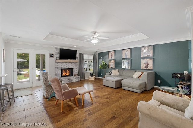 living room featuring a fireplace, wood-type flooring, ceiling fan, a tray ceiling, and crown molding