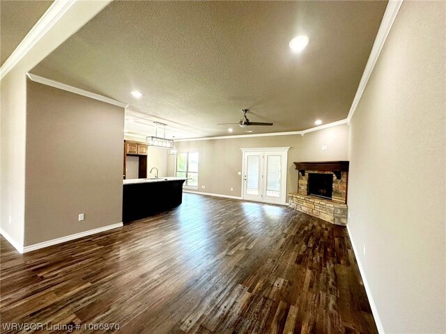 unfurnished living room with dark wood-type flooring, a stone fireplace, sink, crown molding, and ceiling fan