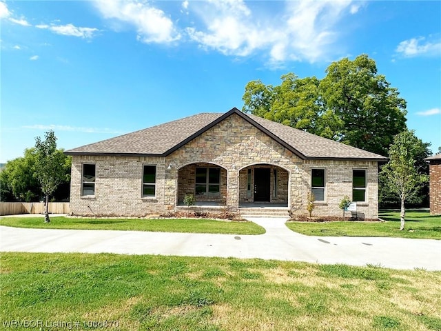 french country home featuring covered porch and a front lawn