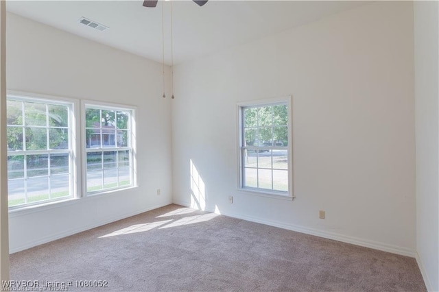 carpeted spare room featuring baseboards, a wealth of natural light, visible vents, and a ceiling fan