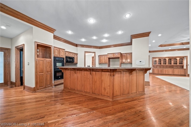 kitchen featuring a spacious island, crown molding, black appliances, wood-type flooring, and a breakfast bar area