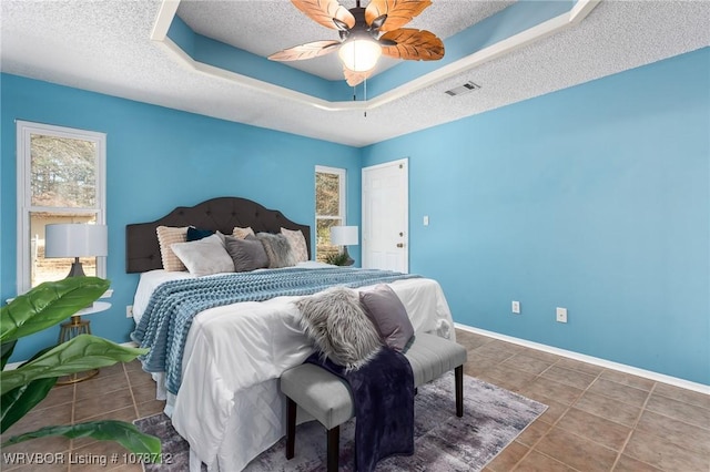 bedroom featuring ceiling fan, a tray ceiling, dark tile patterned floors, and a textured ceiling