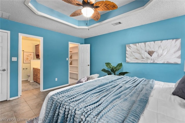 tiled bedroom with ceiling fan, ensuite bathroom, a raised ceiling, and a textured ceiling