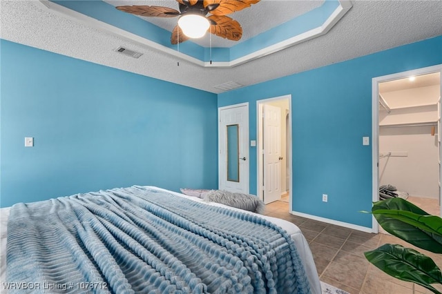 bedroom with tile patterned floors, a skylight, a textured ceiling, a tray ceiling, and ceiling fan