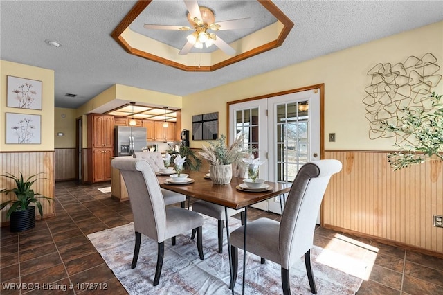 dining room featuring a raised ceiling, ceiling fan, wooden walls, and a textured ceiling