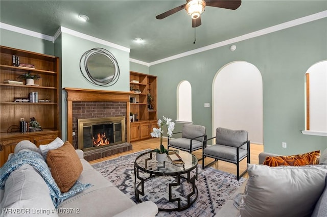 living room featuring a brick fireplace, light hardwood / wood-style flooring, ornamental molding, and ceiling fan