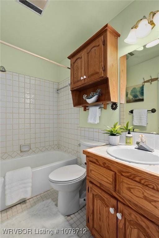 full bathroom featuring tile walls, vanity, tiled shower / bath, tile patterned floors, and toilet