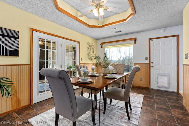 dining space featuring french doors, wood walls, a textured ceiling, a raised ceiling, and ceiling fan