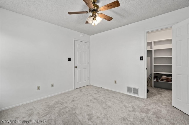 unfurnished bedroom with ceiling fan, a textured ceiling, light carpet, a spacious closet, and a closet