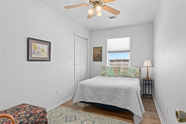 bedroom with ceiling fan, wood finished floors, visible vents, baseboards, and a closet