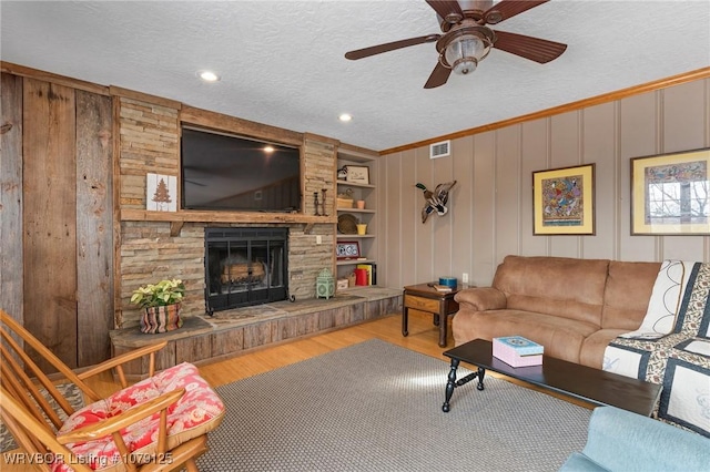 living room featuring a fireplace, visible vents, ceiling fan, a textured ceiling, and wood finished floors