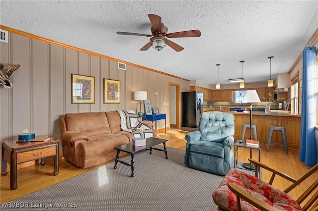 living area with light wood-style floors, visible vents, a textured ceiling, and ornamental molding