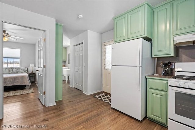 kitchen with white appliances, under cabinet range hood, green cabinets, and light wood finished floors