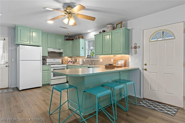 kitchen featuring a peninsula, white appliances, light countertops, and under cabinet range hood