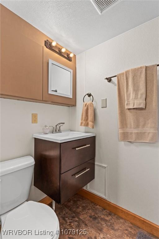 bathroom featuring a textured ceiling, toilet, vanity, visible vents, and baseboards