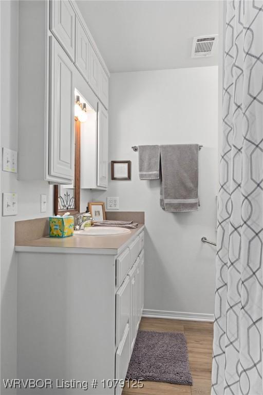 full bath featuring curtained shower, visible vents, vanity, wood finished floors, and baseboards