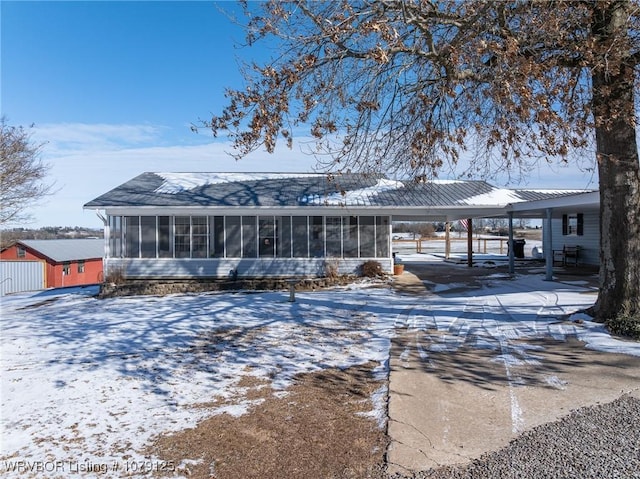 snow covered rear of property featuring driveway, a sunroom, and a carport