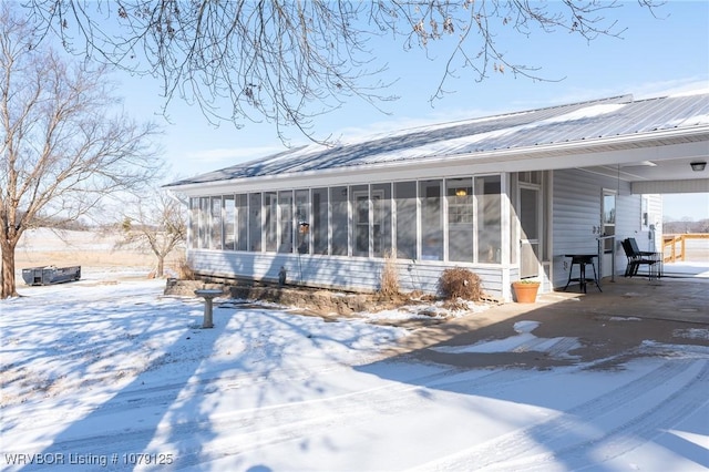 snow covered rear of property featuring metal roof and a sunroom