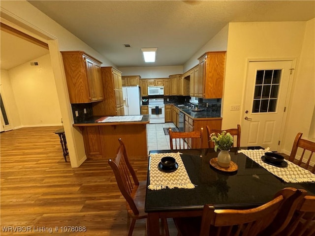 kitchen featuring sink, tasteful backsplash, kitchen peninsula, light hardwood / wood-style floors, and white appliances