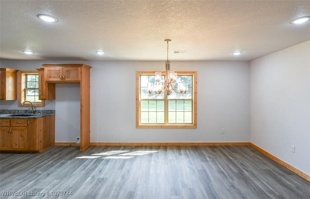 unfurnished dining area featuring a textured ceiling, sink, a chandelier, and dark hardwood / wood-style floors